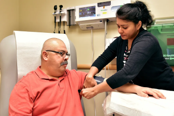 A Veteran sits in an exam room as a provider takes their blood pressure. 