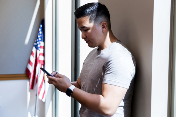 A Veteran leaning against a wall in a VA facility while reading information on their phone