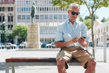 A Veteran sits on a bench outside and uses the VA health chat app on the phone.