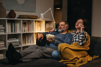 Two people sitting on a sofa together eating popcorn. 