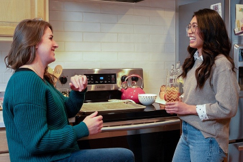 Two people chat in the kitchen. 