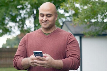 A person standing outside looks down at their phone.