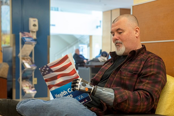 A Veteran with a prosthetic arm reads a health information packet while sitting in a waiting room.