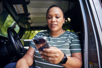 A person sitting in their car looks down at their phone.